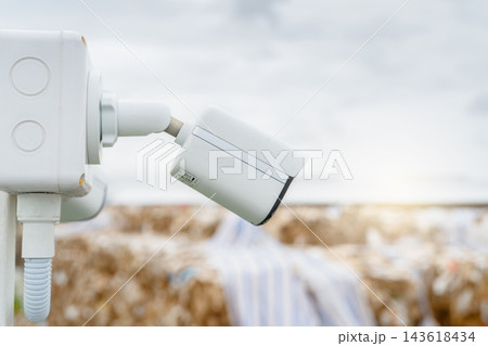White CCTV security camera monitoring a paper recycling factory outdoors in daylight, video surveillance system protecting industrial operations, property, workers and recyclable material White CCTV security camera monitoring a paper recycling factory outdoors in daylight, video surveillance system protecting industrial operations, property, workers and recyclable material 143618434
