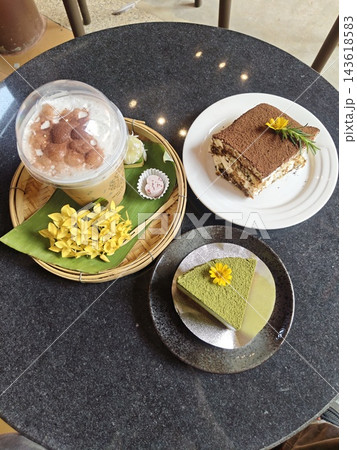 A satisfying assortment of desserts: Tiramisu, Matcha Mousse, and a creamy smoothie with fresh flowers on a dark textured table, ready for a cozy afternoon treat. A satisfying assortment of desserts: Tiramisu, Matcha Mousse, and a creamy smoothie with fresh flowers on a dark textured table, ready for a cozy afternoon treat. 143618583
