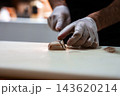 A chef in white gloves slices squid or scallop on a white cutting board in a Maldives professional kitchen. Soft, shallow focus lighting isolates hands and knife. 143620214