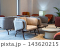 Clusters of gray, beige, and rust armchairs sit by round tables on layered rugs in Male, Maldives. Soft diffused light from a tall window and a textured lamp adds calm. 143620215