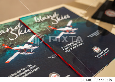 Two glossy Island Skies magazines rest on a table in Male, covers show a red and white seaplane over turquoise reefs, TMA badge visible, warm indoor lighting. Two glossy Island Skies magazines rest on a table in Male, covers show a red and white seaplane over turquoise reefs, TMA badge visible, warm indoor lighting. 143620219