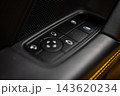 Tight close up of a Porsche 911 Carrera door switch panel with black window, mirror pad, and lock buttons beside a perforated speaker and yellow stitched leather trim. 143620234