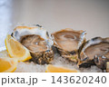 Three opened raw oysters sit chilled on crushed ice alongside sliced fresh lemon wedges ready to eat in a restaurant setting. 143620240