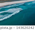 Aerial view shows rolling turquoise waves curling toward a long pale sand beach on Cape Town Atlantic coast, white foamy breakers stripe water in late day light. 143620242