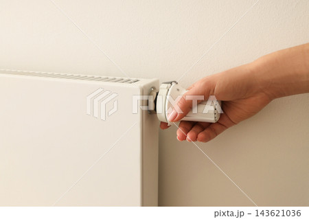 A hand is turning the valve on a white radiator for warmth 143621036
