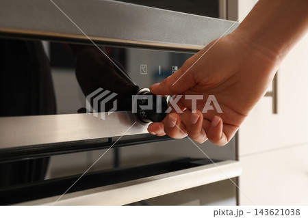 Hand adjusting the oven temperature dial in a stylish kitchen Hand adjusting the oven temperature dial in a stylish kitchen 143621038