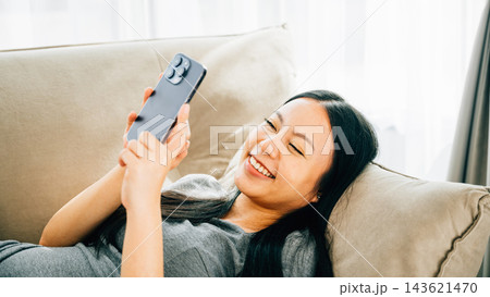 Young woman on a comfortable sofa uses her smartphone for texting chatting and online shopping Young woman on a comfortable sofa uses her smartphone for texting chatting and online shopping 143621470