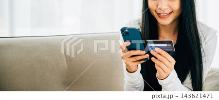 Smiling woman holds smartphone and credit card shops online on sofa Smiling woman holds smartphone and credit card shops online on sofa 143621471