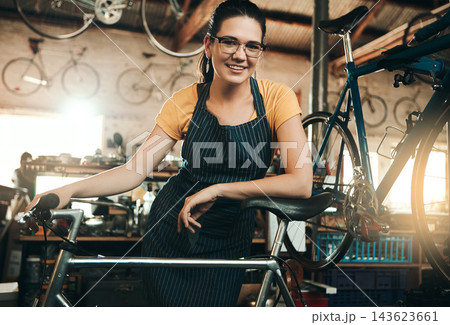 Woman, bicycle shop and portrait for maintenance job, startup with transport service. Bike, mechanic and female entrepreneur in workshop with glasses, happiness for sustainable business with apron 143623661