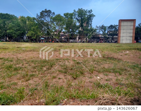 Empty dirt and grass field overlooking a street with trees, motorbikes, and a blank sign. 143626067