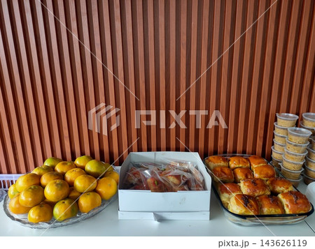 Catering food spread featuring oranges, wrapped savory snacks, and baked buns on a table Catering food spread featuring oranges, wrapped savory snacks, and baked buns on a table 143626119