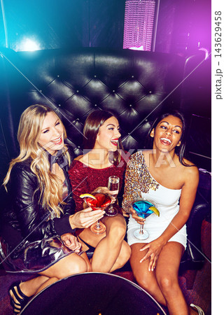 Women, happy and friends in nightclub with cocktails, drink or glass for vip, event or reunion. Smile, relax and people in dark disco party couch for fashion, alcohol or social celebration in group 143629458