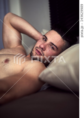 Shirtless man, sensual and portrait with bed, bedroom and lazy morning with sexy look. Guy, waking up and seductive with desire, comfort and handsome topless dude with natural body for weekend break 143629989