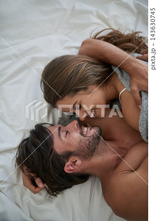Couple, cuddle and smile in bed for morning romance, love and bonding on weekend. Relationship, man and woman laying together in home for comfort, relax or care and playing with partner from above Couple, cuddle and smile in bed for morning romance, love and bonding on weekend. Relationship, man and woman laying together in home for comfort, relax or care and playing with partner from above 143630745