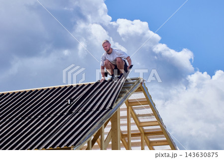 Bitumen corrugated roofing sheets installed on wooden roof framework by construction worker. Bitumen corrugated roofing sheets installed on wooden roof framework by construction worker. 143630875