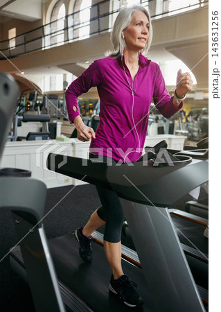 Woman, running on treadmill and training by music in gym club, breathing and cardio for health in wellness. Mature, female runner and exercise with podcast, athlete and workout by speed machine 143631256