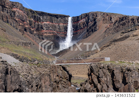 Hengifoss waterfall and hiking bridge beneath red basalt cliffs in summer Iceland Hengifoss waterfall and hiking bridge beneath red basalt cliffs in summer Iceland 143631522