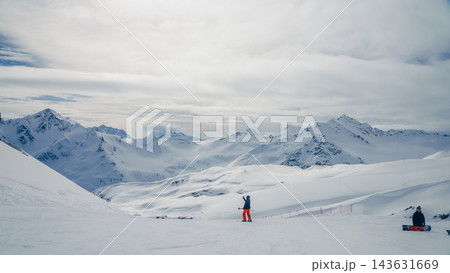 Skier waving from snowy ridge with panoramic view of alpine peaks under overcast sky 143631669