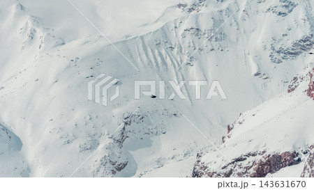 Aerial snow-covered slope with rocky outcrops and wind-sculpted cornices on mountain 143631670