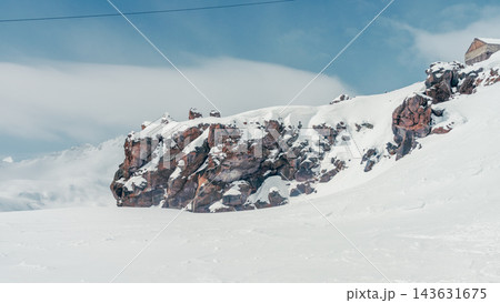 Snow-covered rocky outcrop on alpine slope near Mount Elbrus under pale blue sky 143631675