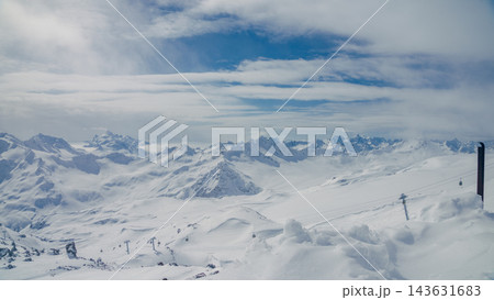 Snow-covered Caucasus mountain panorama with cable cars over glacier and distant jagged peaks under layered cloud sky Snow-covered Caucasus mountain panorama with cable cars over glacier and distant jagged peaks under layered cloud sky 143631683