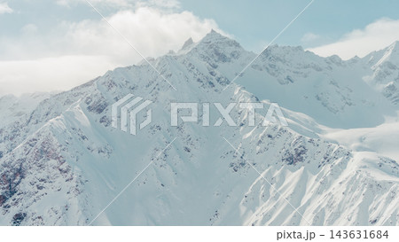 Snow-covered high mountain peaks with steep ridges and wind-scoured slopes under pale blue sky Snow-covered high mountain peaks with steep ridges and wind-scoured slopes under pale blue sky 143631684