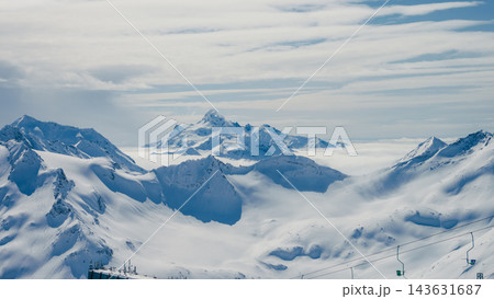 Panoramic snow-covered Caucasus peaks with ridge, cloud inversion, and ski lift in foreground near Mount Elbrus nightless length 1 143631687
