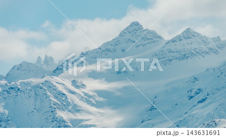 Snow covered mountain peaks and glacier slopes under pale blue sky with scattered clouds 143631691