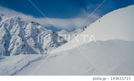 Mount Elbrus snow-covered ridge and distant Caucasus peaks under clear blue sky, pristine alpine powder slope in foreground 143631715