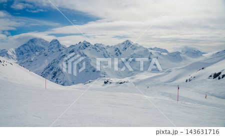 Panoramic snow-covered Mount Elbrus and surrounding Caucasus peaks with groomed ski slope and marker poles Panoramic snow-covered Mount Elbrus and surrounding Caucasus peaks with groomed ski slope and marker poles 143631716