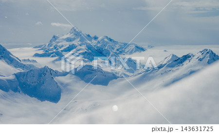 Snow-covered Mount Elbrus and surrounding Caucasus ridges rising above clouds in blue winter daylight 143631725