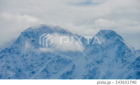 Snow-covered peaks of Mount Elbrus in Caucasus Mountains with low cloud over rugged alpine ridgeline Snow-covered peaks of Mount Elbrus in Caucasus Mountains with low cloud over rugged alpine ridgeline 143631740