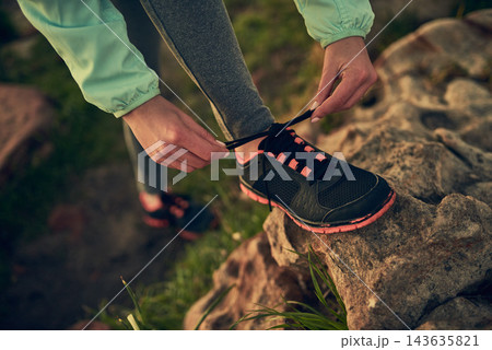 Person, hands and tying shoe with rock of hiker for morning walk or trekking on outdoor mountain. Closeup of human getting ready, preparation or tie laces for hiking, journey or exercise in nature Person, hands and tying shoe with rock of hiker for morning walk or trekking on outdoor mountain. Closeup of human getting ready, preparation or tie laces for hiking, journey or exercise in nature 143635821