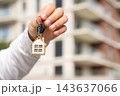 Closeup Of Real Estate Agent Offering Keys With House Keychain Against Blurred Apartment Building. Copy Space For Property Sales And Rental Advertising. 143637066