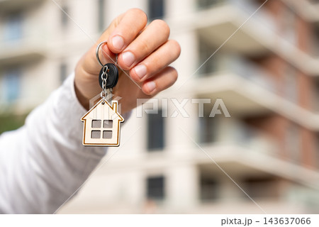 Closeup Of Real Estate Agent Offering Keys With House Keychain Against Blurred Apartment Building. Copy Space For Property Sales And Rental Advertising. 143637066
