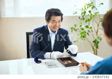 貴金属を査定する買取専門業者とシニア女性 貴金属を査定する買取専門業者とシニア女性 143637142