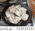 Preparing breaded fish fillets, coated in white flour, for frying in a hot cast iron skillet on a gas stove, illustrating home cooking and a healthy meal 143638342
