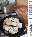 Fish fillets coated in flour cooking in a hot cast iron frying pan on a gas stove burner next to a lidded pot, preparing a delicious seafood meal 143638348