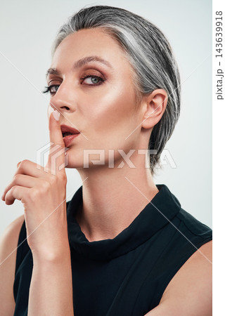 Portrait, mature woman and studio with secret hand sign for privacy, silence and gossip on white background. Female person, whisper and quiet gesture for rumor, mystery and confidentiality or hush 143639918