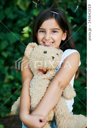 Outdoor, portrait and girl with teddy bear, toys and hug with safety and security in home garden. Calm, kid and child relax with smile on face and embrace soft doll in backyard with happiness 143641019