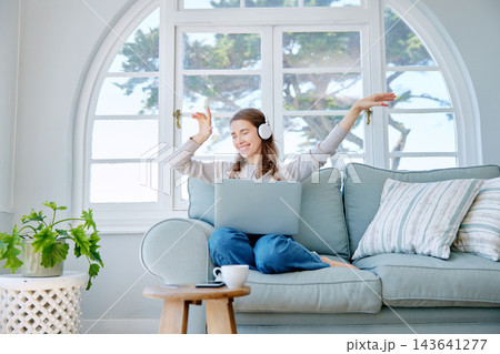 Woman, laptop and headphones for dancing in home, freelancer and online for copywriter research on sofa. Female person, playlist and relax on couch, website and planning or listening to sound or song 143641277