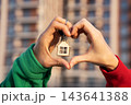 Closeup Of Couple Making Heart Shape With Hands Around House Keychain With Keys, Apartment Building Background. Real Estate, Home Purchase, Mortgage, Achievement Concept 143641388