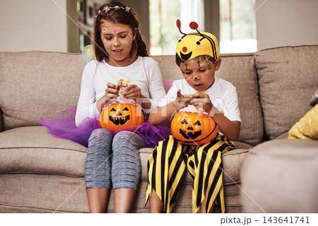 Halloween, sweets and children on sofa with costume for holiday event, celebration and happiness with pumpkin. Couch, young girl and boy with orange vegetable for eating candy, smile and fairy outfit 143641741