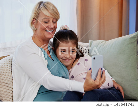 Grandma, kid and smile with selfie on sofa for family bonding, care or memory in living room. Home, girl and elderly woman with digital photography for support, happiness or love in child development Grandma, kid and smile with selfie on sofa for family bonding, care or memory in living room. Home, girl and elderly woman with digital photography for support, happiness or love in child development 143641743