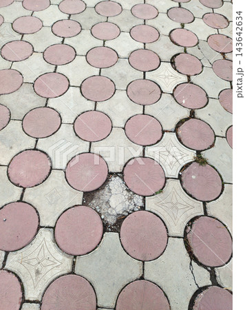 Outdoor paved walkway featuring a geometric tessellation of circular pink-red and star-patterned grey concrete tiles. The aged surface shows wear, cracks, and weeds in the joints. 143642634