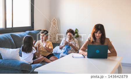 Children playing while grandmother knitting and mother working on laptop Children playing while grandmother knitting and mother working on laptop 143642879