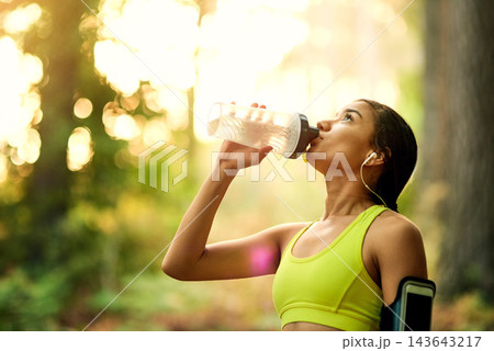 Running, fitness and woman drinking water in park with earphones for wellness, workout and training in nature with radio. Sports, liquid and thirsty runner with refreshing drink in forest for cardio 143643217
