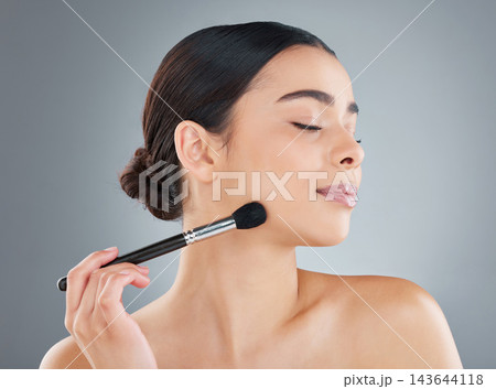 Young woman, gray background and beauty with blusher for facial transformation, skincare or cosmetic. Female person, studio and smile with tool on cheek for wellness, glow and shine with eyes closed Young woman, gray background and beauty with blusher for facial transformation, skincare or cosmetic. Female person, studio and smile with tool on cheek for wellness, glow and shine with eyes closed 143644118