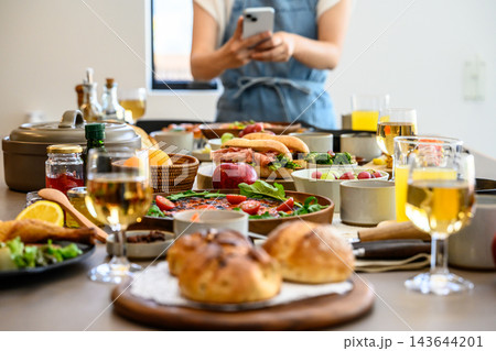 スマートフォンで料理を撮影する女性と彩り豊かな食卓 143644201