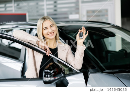 Happy business woman showing car key in dealership Happy business woman showing car key in dealership 143645086